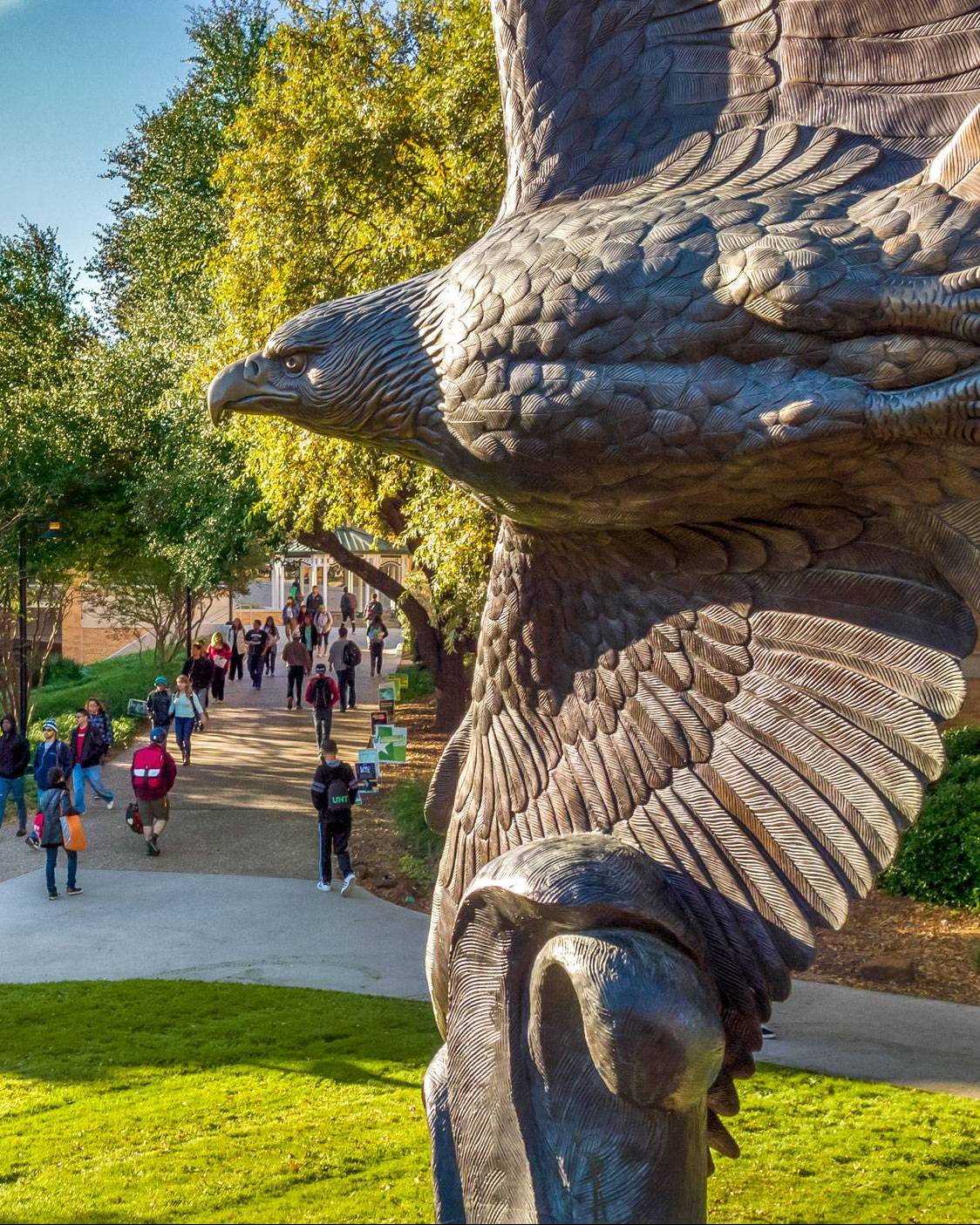 large bronze eagle statue with its wings spread, overlooking a busy campus walkway
